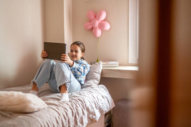 istock Happy young girl is using a digital tablet while sitting comfortably on her bed in a cozy bedroom, enjoying online entertainment or educational resources 2198755877