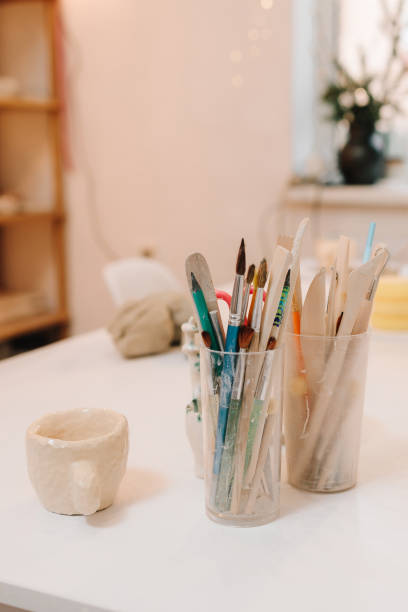 istock Creative atmosphere for designing ceramic crockery with paintbrushes and handmade ceramic cup on the table. Cozy art studio with sculpting tools. 2198758962