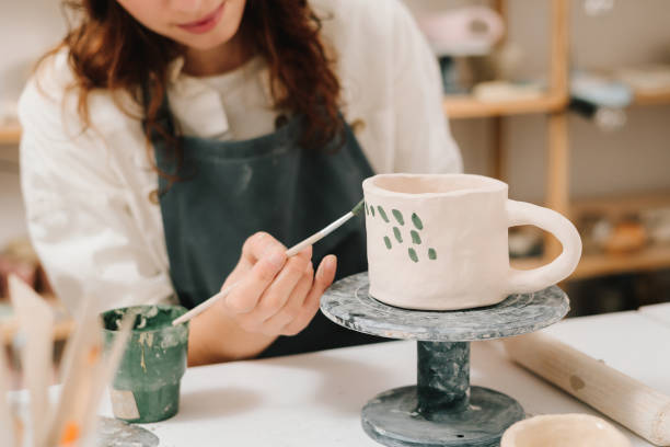 istock Process of designing cup with a traditional pattern in pottery art studio. Artisan stamps decorative symbols on the dry clay of the cup. 2198761585