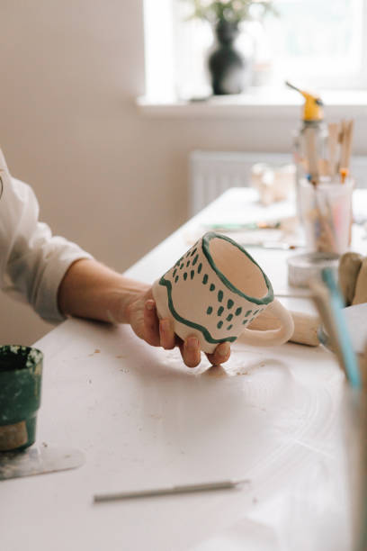 istock Experienced artist painting designs on ceramic cup in pottery workshop. Potter draws an abstract design into earthenware cup. 2198761996
