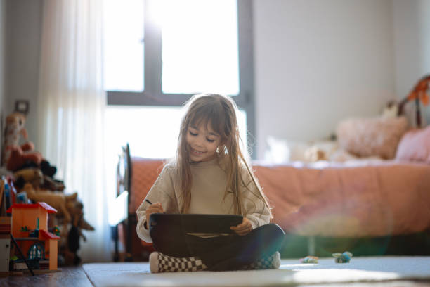 Happy little girl using tablet drawing while sitting on the floor Little girl keeping herself entertained with the online world. Happy little girl enjoying while watching cartoons on digital tablet at home how to draw a house step by step for kids cartoon stock pictures, royalty-free photos & images
