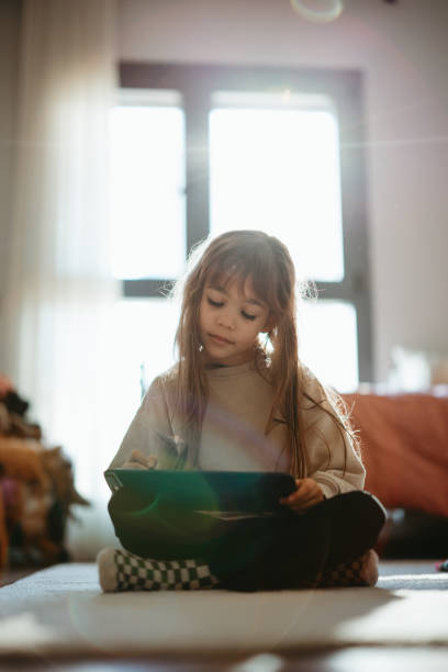 Happy little girl using tablet drawing while sitting on the floor Little girl keeping herself entertained with the online world. Happy little girl enjoying while watching cartoons on digital tablet at home how to draw a house step by step for kids cartoon stock pictures, royalty-free photos & images