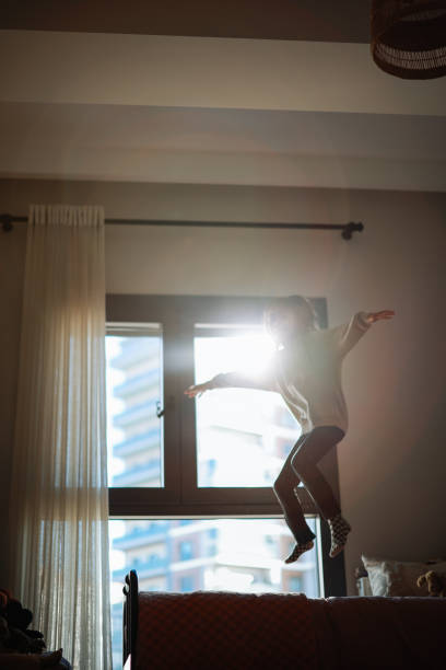 istock Happy funny child girl jumping on bed alone feeling joy 2198765250