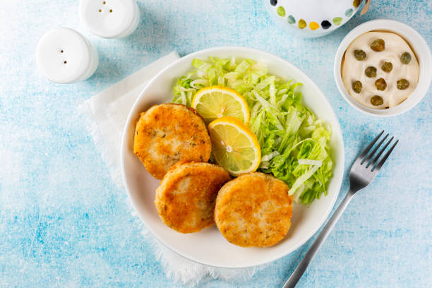 Fish cakes or fish burger made from ground perch and tuna with herbs, iceberg salad, lemon slice. Top view.