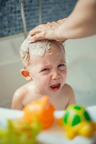Crying baby getting hair washed in bathtub by mother stock photo