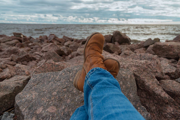 two legs of women in blue jeans trousers, natural boots on rocky beach by sea