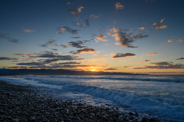 istock Serene sunset over the ocean with gentle waves crashing on a rocky shore 2198772003