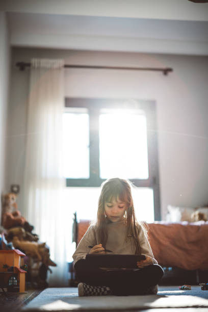 Happy little girl using tablet drawing while sitting on the floor Little girl keeping herself entertained with the online world. Happy little girl enjoying while watching cartoons on digital tablet at home how to draw a house step by step for kids cartoon stock pictures, royalty-free photos & images
