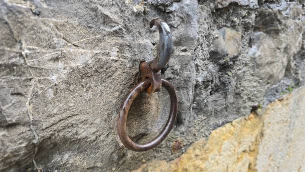 istock A rusty metal ring attached to an old stone wall via a weathered hook. The aged appearance suggests it may have been used for tethering animals or securing objects in the past. 2198774496