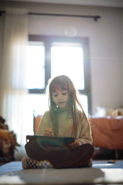 Happy little girl using tablet drawing while sitting on the floor Little girl keeping herself entertained with the online world. Happy little girl enjoying while watching cartoons on digital tablet at home how to draw a house step by step for kids cartoon stock pictures, royalty-free photos & images