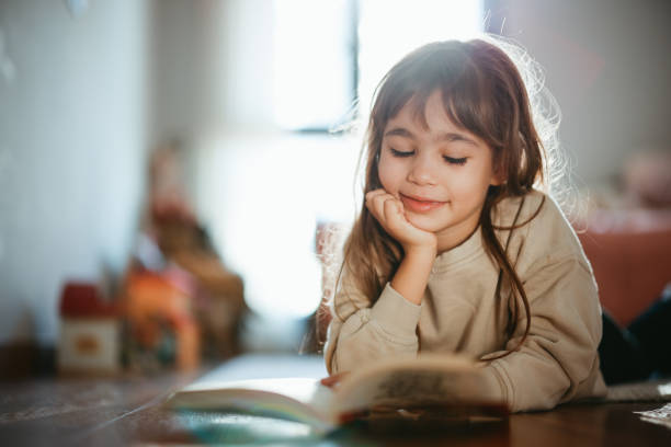 istock Beautiful little girl reading book lying on the carpet 2198775665