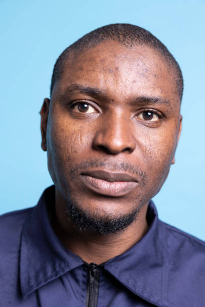 Portrait of serious security officer in professional uniform on camera, feeling proud of his responsibility against blue background. Young bodyguard working on protecting the premises. Close up.