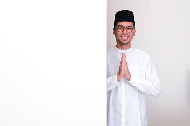 istock Muslim man standing behind a blank board doing greeting with happy face 2198783451