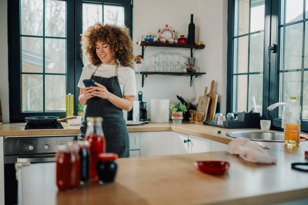 ผู้หญิงใช้สมาร์ทโฟนและยิ้มขณะทําอาหารในครัว