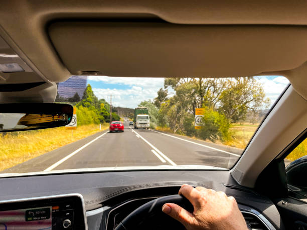 istock A wide-angle view through a car’s windscreen reveals a highway through a desert plain, framed by the interior, steering wheel, and driver’s hands under a clear blue sky with fluffy clouds 2198785817