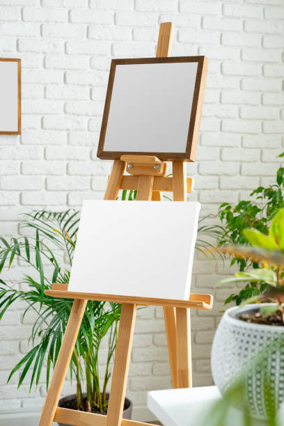 istock Blank canvas on wooden easel surrounded by indoor plants in a bright, minimalist studio space 2198787689