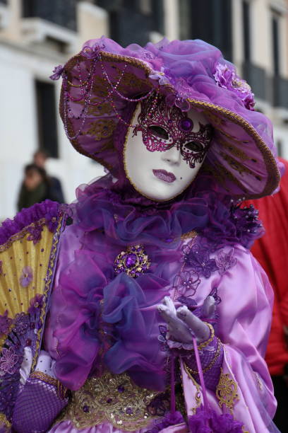 Venice, Italy - February 24, 2014: The photo was taken during the famouse carnival in front the church San Giorgio Maggiore in Venice. We can see attractive person who wearing traditional carnival costume with butterfly wigs in black and purple colors. Doges Palace and Campanile are on the background. Venice, Italy, Europe.