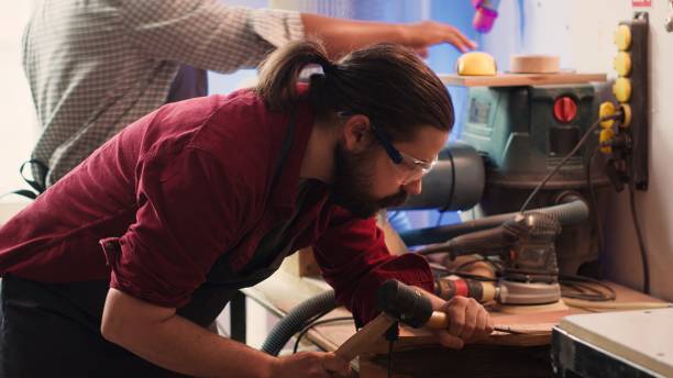 istock Man carves intricate designs into wood using chisel and hammer in carpentry shop 2198788342