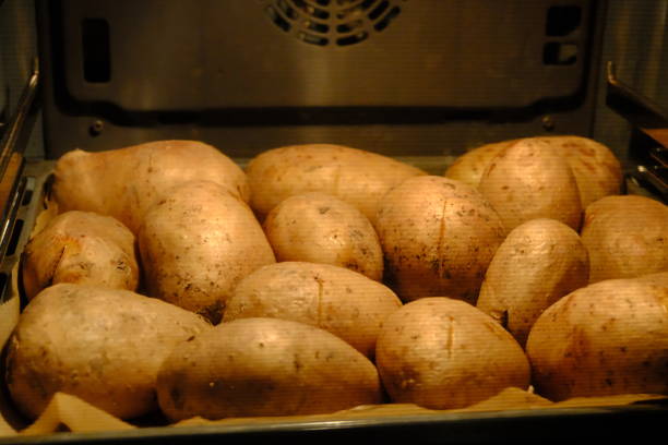 View of raw potatoes cooking in the oven. Baked potatoes. Making baked potatoes at home. Vegan diet. Diet, healthy eating. Black background. Built-in oven.