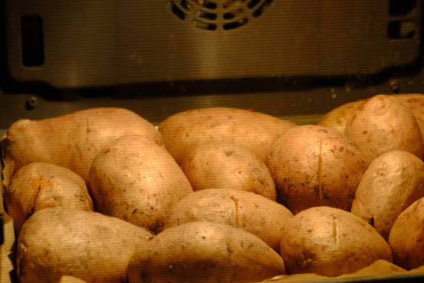 View of raw potatoes cooking in the oven. Baked potatoes. Making baked potatoes at home. Vegan diet. Diet, healthy eating. Black background. Built-in oven.
