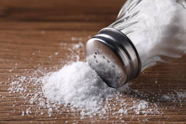istock Overturned shaker with salt on wooden table, closeup 2198802935