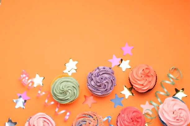 Delicious cupcakes with bright cream and party decor on orange background, flat lay. Space for text