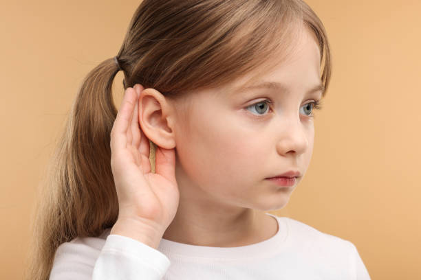 istock Little girl with hearing problem on pale brown background 2198807816