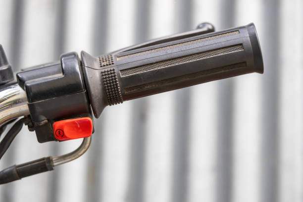 Close-up of a motorcycle handlebar with a red push-button for electric start. This button is used to ignite the motorbike.
