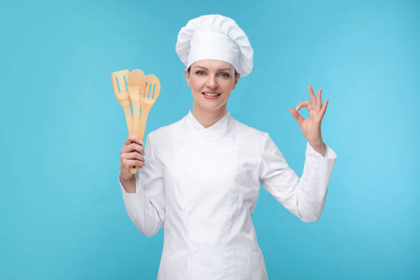 istock Happy chef in uniform holding wooden utensils on light blue background 2198812525
