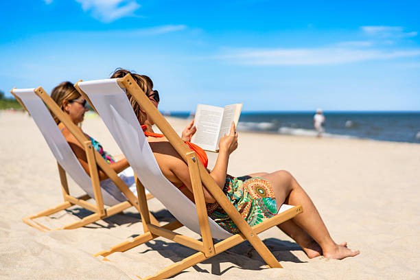 istock Two mature women reading books sitting on deckchairs on beach 2198830590