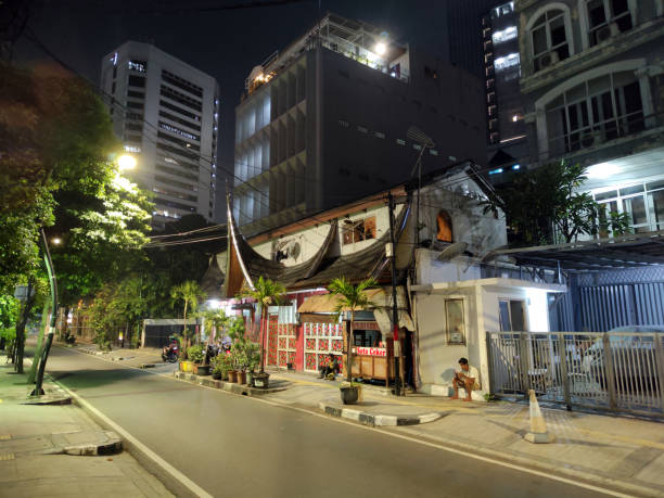 Two people sitting by an old house at night in Jalan Jaksa, once a famous tourist hub street in Central Jakarta, Indonesia.