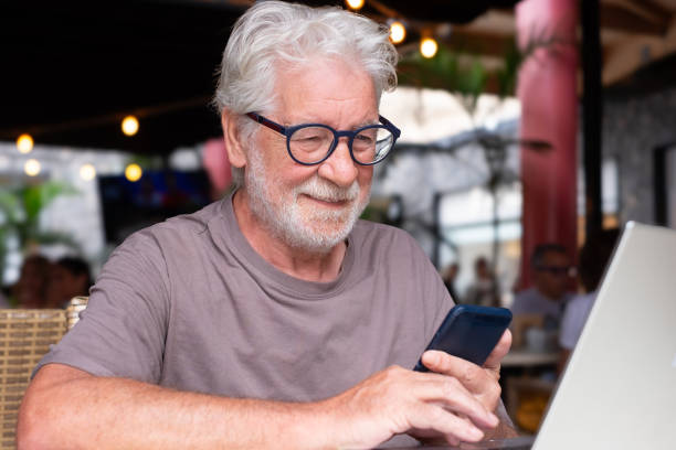 istock Attractive senior man sitting in a cafe smiling while using mobile phone. Cheerful senior male, using modern technology expressing happiness and contentment in a relaxed atmosphere 2198838895
