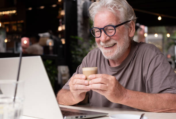 istock Attractive cheerful senior man sitting in a cafe using laptop while enjoying a break with a coffee. Modern and smiling elderly man surfing the net in a relaxed atmosphere 2198838958