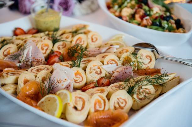 A platter of gourmet rolled appetizers with salmon, dill, and lemon slices, accompanied by a fresh salad in the background.