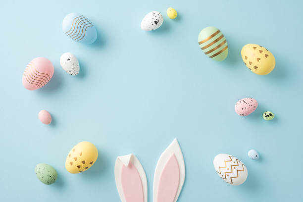istock Colorful pastel Easter eggs arranged around pink bunny ears on a soft blue backdrop 2198847725