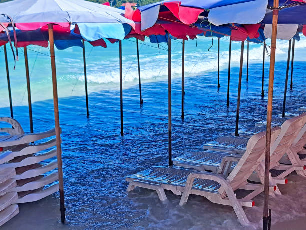 View on empty sunbeds under textile umbrellas is flooded with sea waves on tropical beach