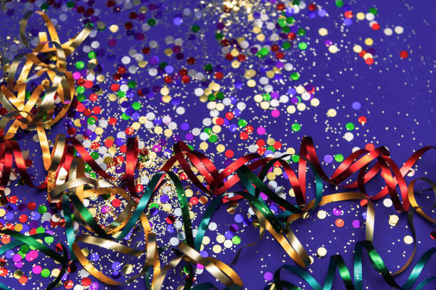 Multi-colored tinsel and confetti on a purple background. Festive, carnival background. Selective focus. Mardi Gras party, Venice Carnival.