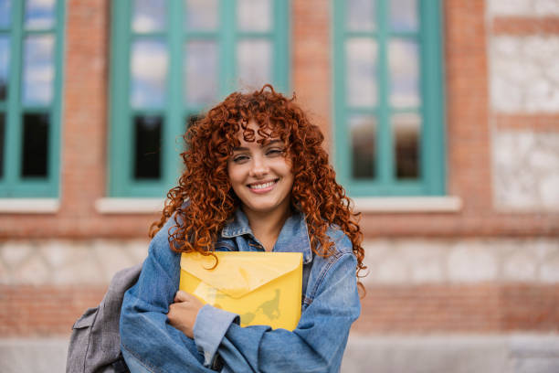 istock Smiling student holding folder in front of university building 2198853300