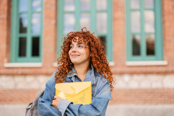 Smiling student holding a yellow envelope in front of school building