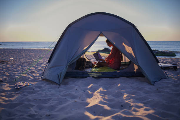At sunrise, a woman works remotely from her beachside tent, laptop open as waves crash nearby. The golden light and ocean breeze create a perfect blend of productivity and serenity.
