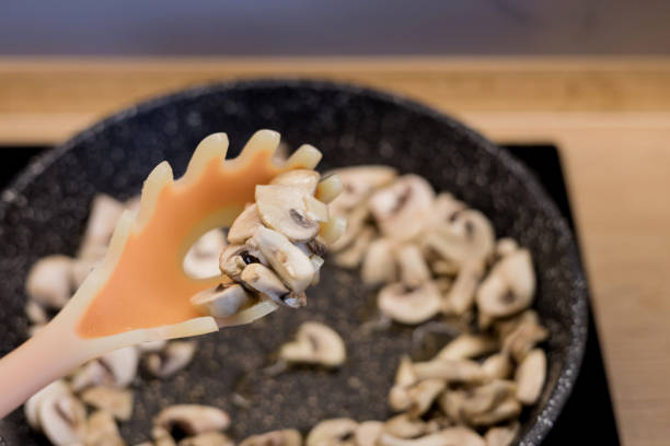 Sliced mushrooms on a cooking spoon with frying pan background, showcasing fresh ingredients and home cooking.