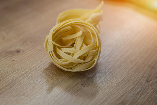 classic Italian raw fettuccine on wooden table. Dry twisted uncooked pasta.