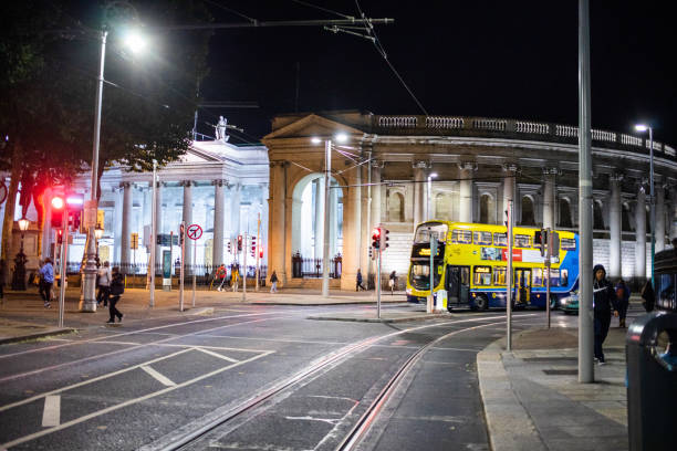 DUBLIN, IRELAND - SEPTEMBER 18, 2018: Pedestrians and vehicles move along a lively Dublin street at night, with a double-decker bus passing a tram station.