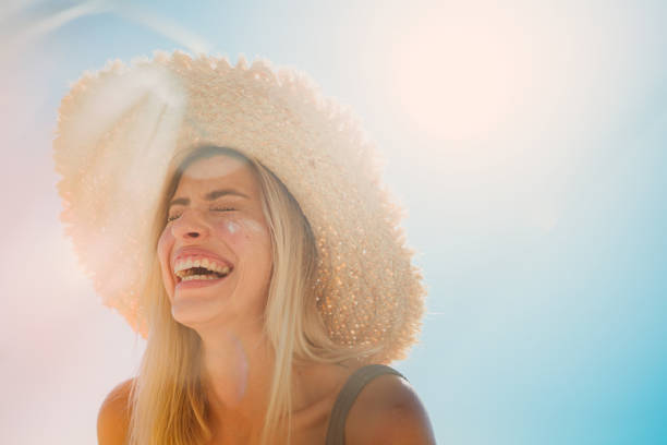 Photo of a young woman applying sunscreen on her face while at the beach
