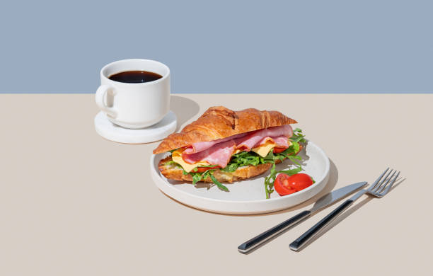 istock Croissant sandwich with ham, cheese, tomato  and arugula on a plate on a light background 2198866359