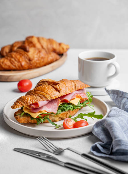 istock Croissant sandwich with ham, cheese, tomato  and arugula on a plate on a light background 2198866456