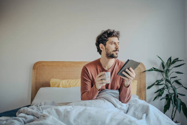 istock Young handsome middle eastern man reading on his tablet or ebook reader and enjoying a cup of coffee or tea. Morning ritual leisure relaxation. 2198868806
