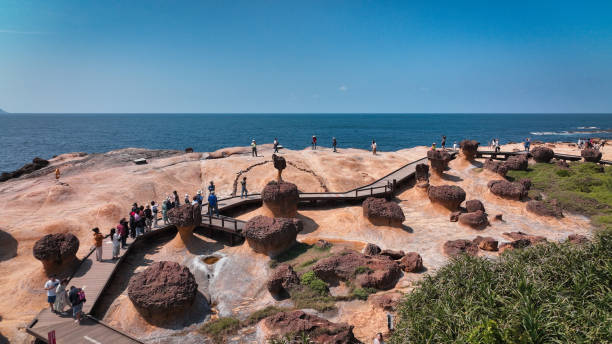 Tourists walk along a wooden boardwalk amidst intriguing rock formations at Yehliu Geopark on a clear day.