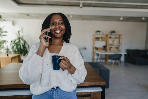 istock Smiling young woman talking on phone and drinking coffee in kitchen 2198884765