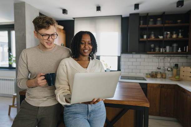 istock Young couple using laptop and drinking coffee in kitchen 2198884822